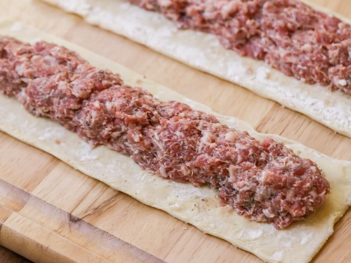 Adding sausage to the center of a puff pastry sheet.