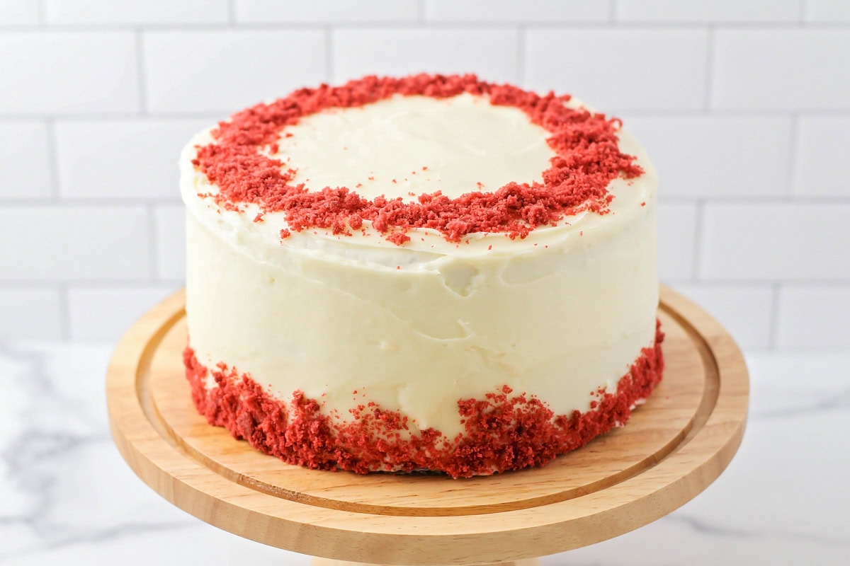 A frosted and decorated red velvet cake on a wooden cake platter.