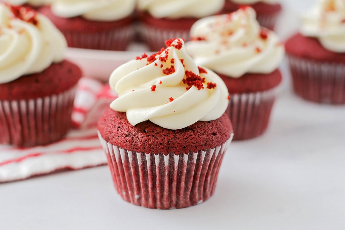 Close up of several frosted red velvet cupcakes on a kitchen counter.