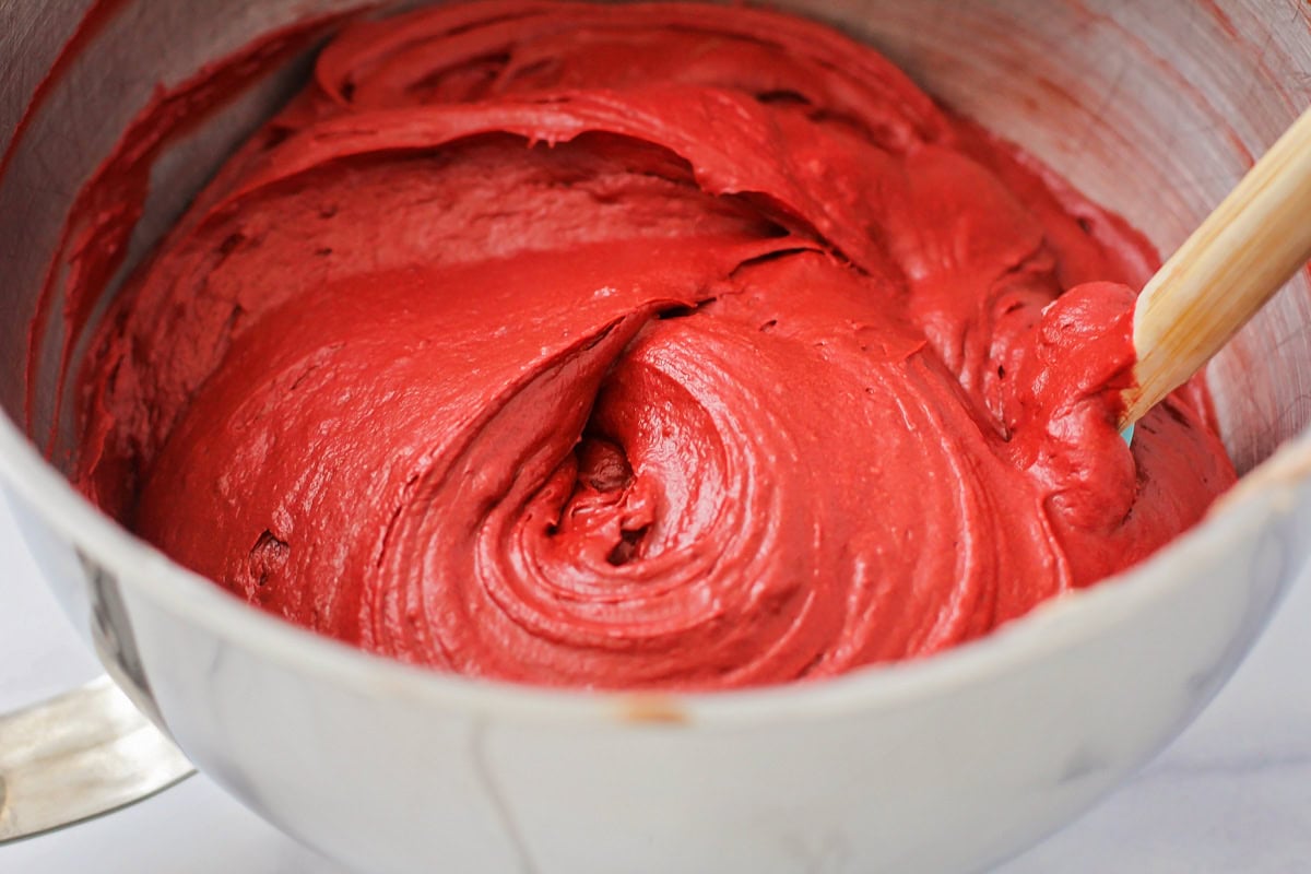 Red cake batter in a metal mixing bowl.