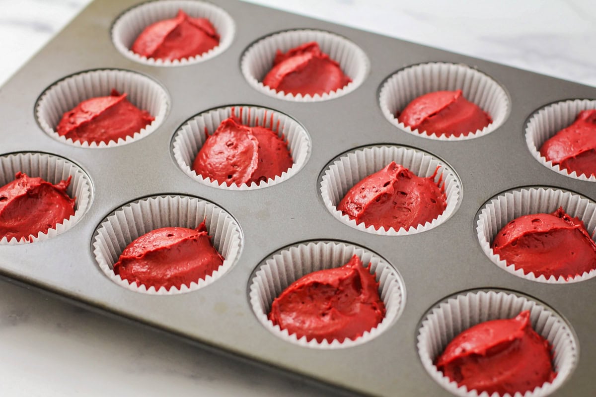 Red cake batter spooned into lined cupcake tin.