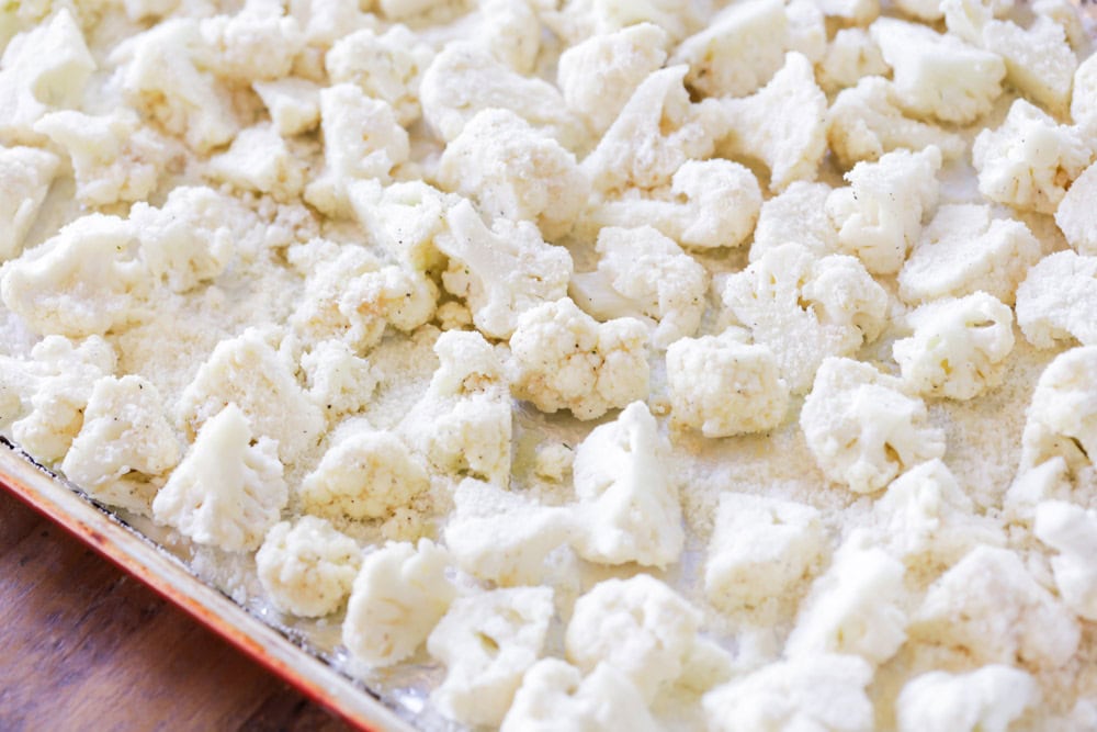 Seasoned cauliflower on a lined baking sheet.