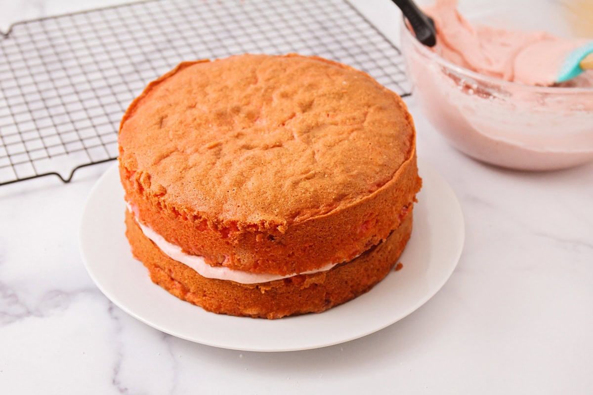 Layering fresh strawberry cake with frosting in between.