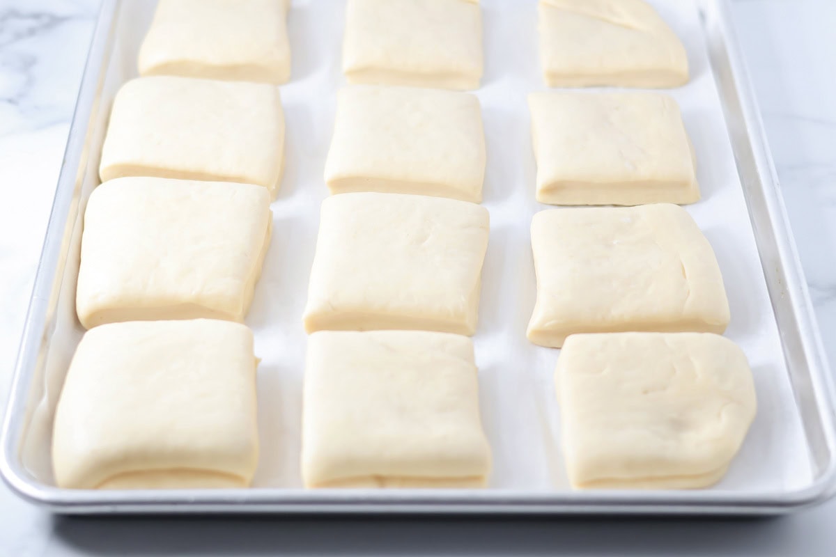 Uncooked squares of roll dough after rising on a baking sheet.