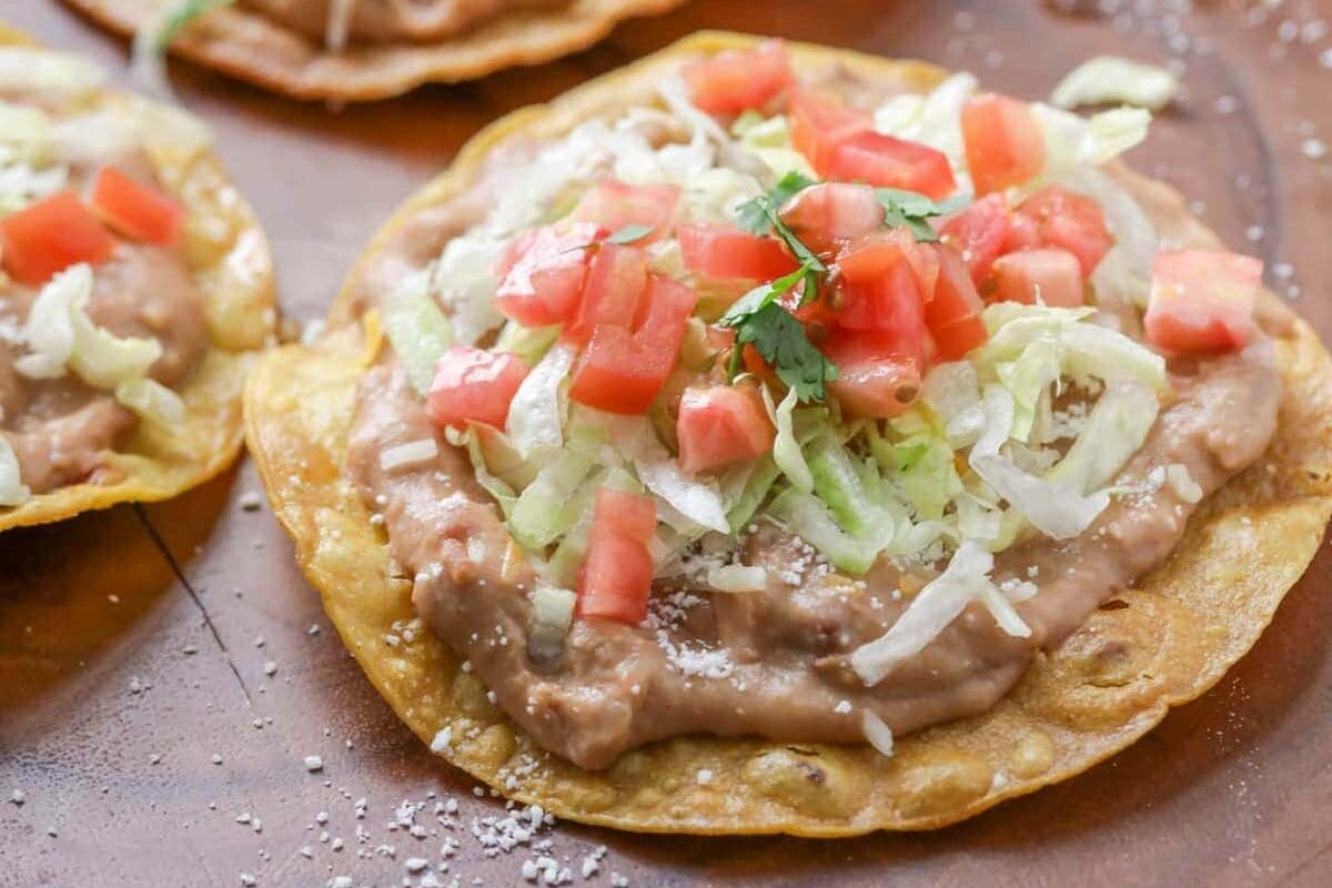 An crunchy open-face tostada is topped with all of your favorite Mexican ingredients and on the table in 20 minutes! Three tostadas topped with refried beans, shredded lettuce, tomatoes, and cheese.