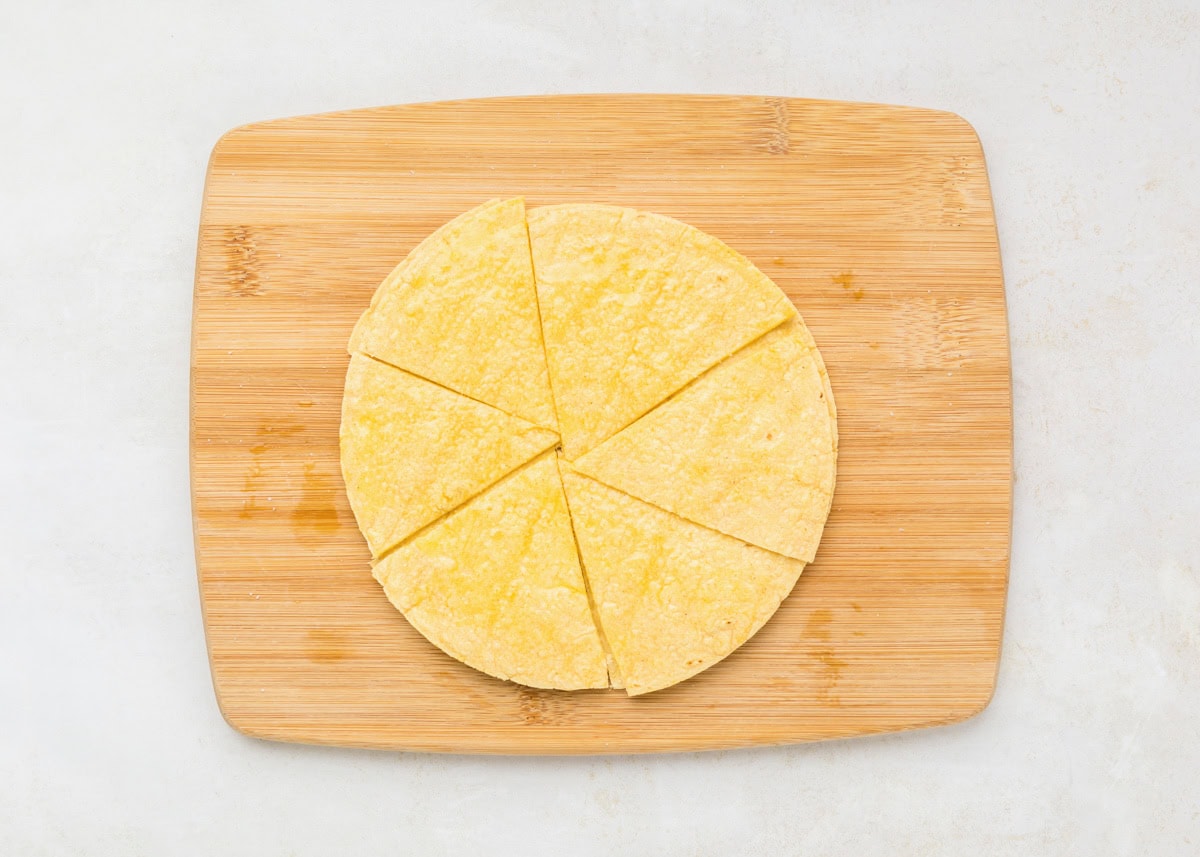A stack of corn tortillas cut into triangles on a wooden cutting board.