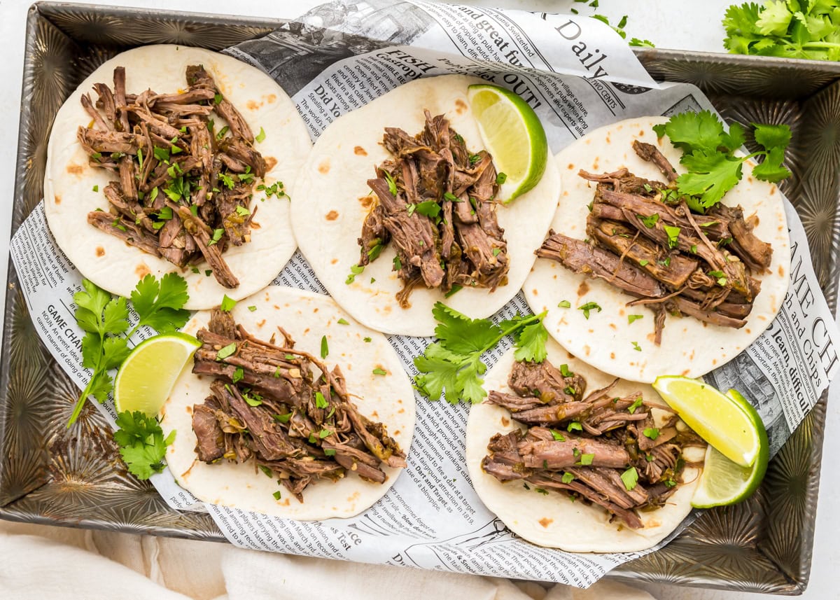 Slow cooker barbacoa on flour tortillas with fresh cilantro and lime.