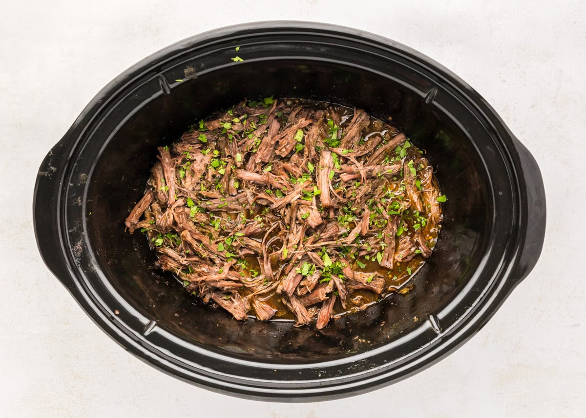 Shredded barbacoa in a crock pot.