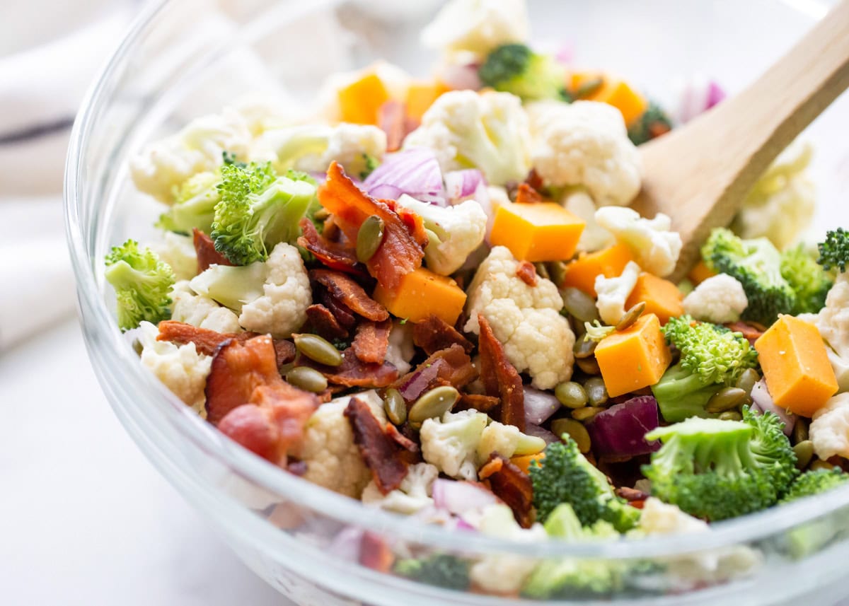 Broccoli, cauliflower, cheese, bacon and more chopped and in glass dish.