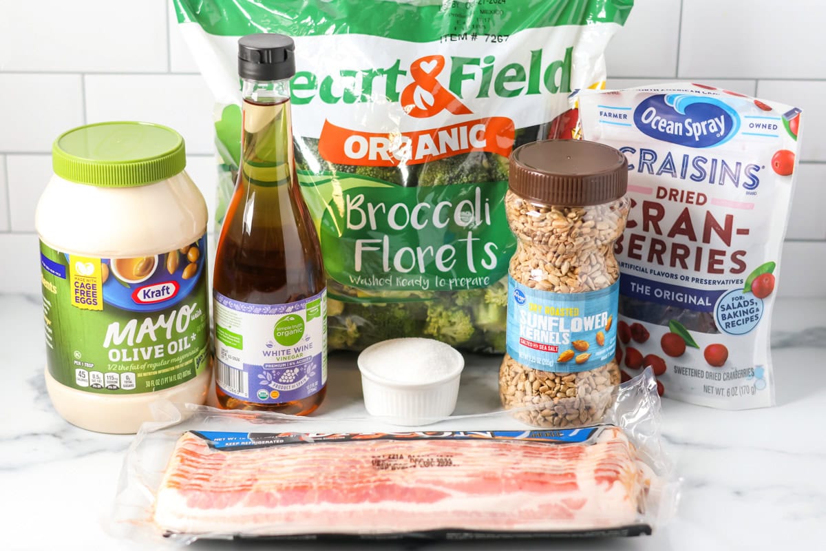 Broccoli, mayo, craisins, sunflower seeds, and other ingredients on a kitchen counter.