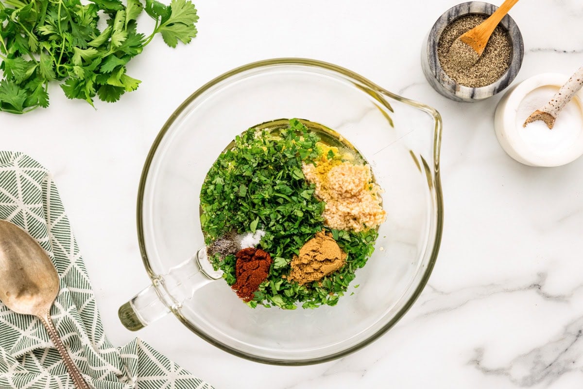 Garlic, cilantro, and seasonings in a glass measuring dish.