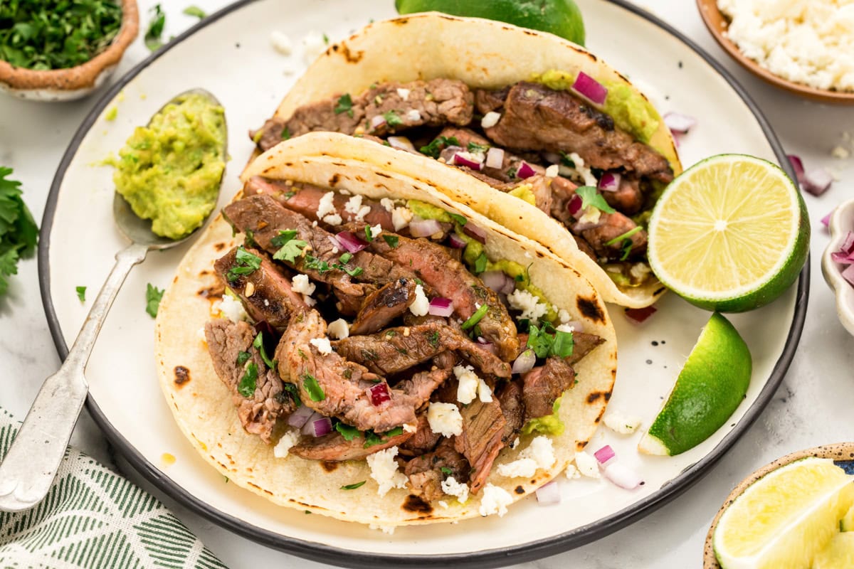 Two carne asada street tacos served on a plate with fresh limes.