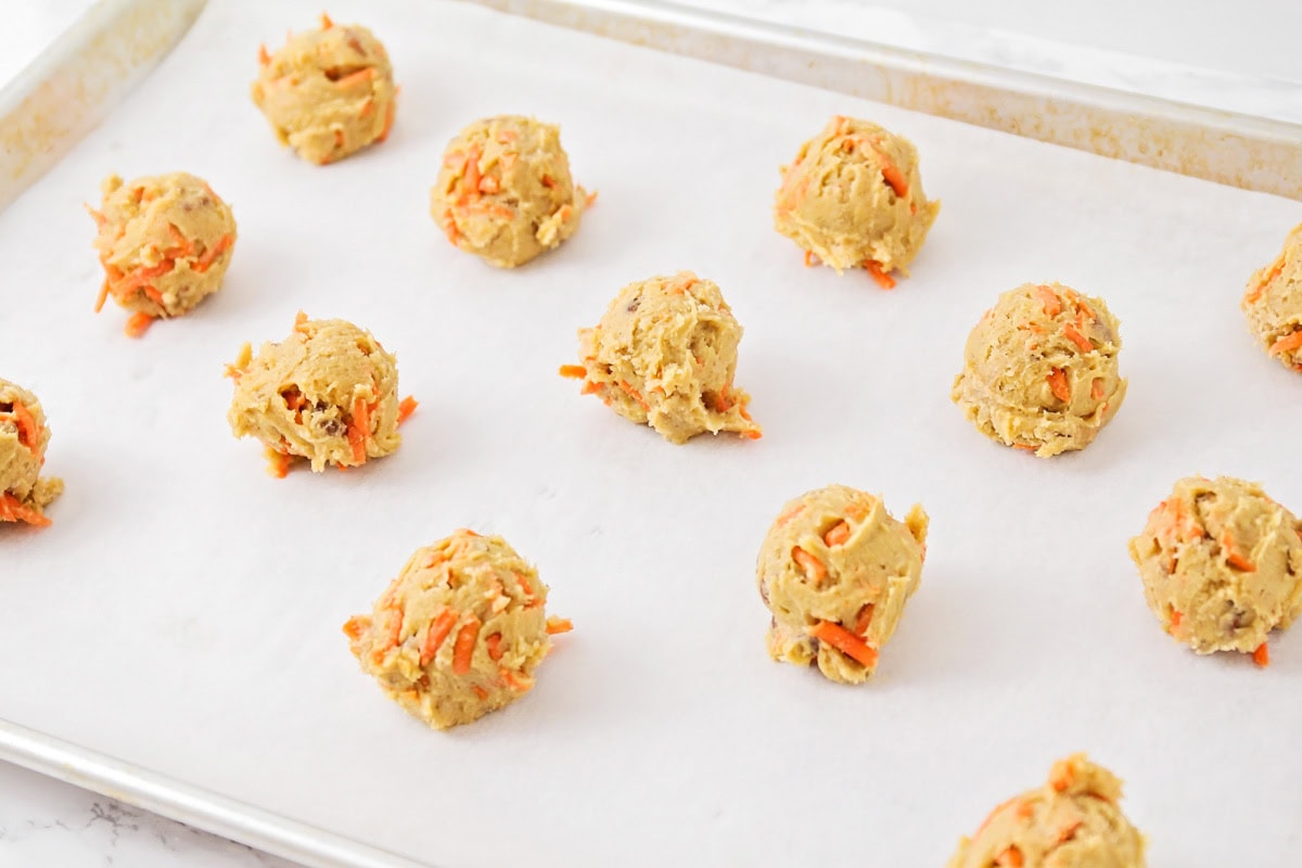 Carrot cake cookie dough scoops on parchment paper lined sheet.