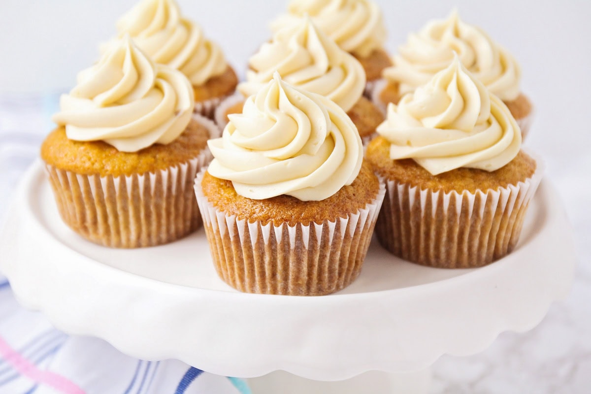 Close up image of carrot cake cupcakes on white cake stand.