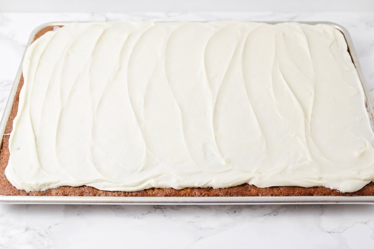 Cream cheese frosting spread onto carrot sheet cake in a jelly roll pan.