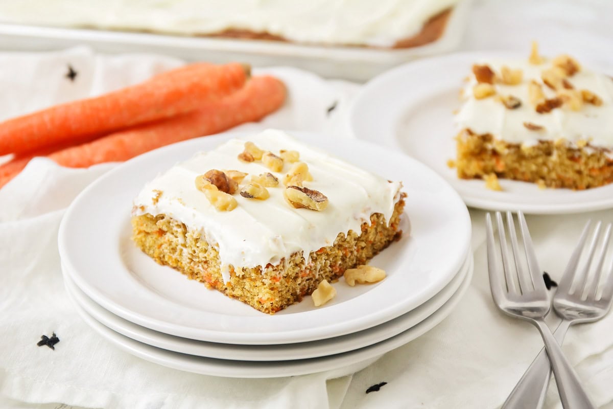 Slice of carrot sheet cake on 3 white plates with forks near by.