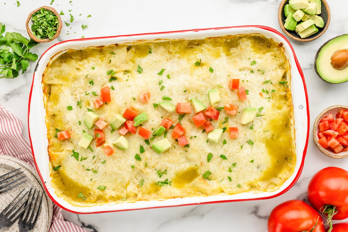 A baked chicken enchilada casserole topped with fresh cilantro and diced avocadoes and tomatoes.