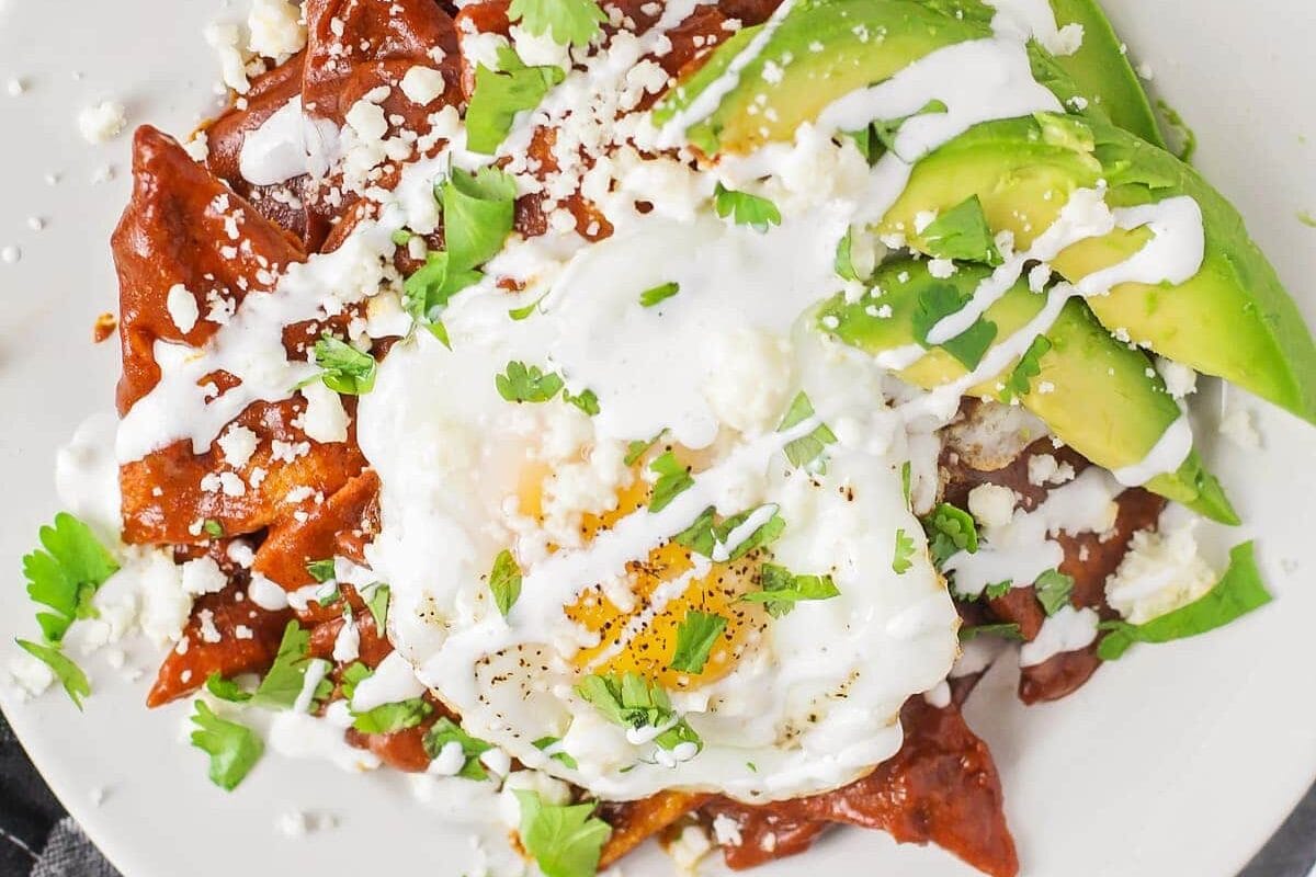 A plate of chilaquiles recipe topped with a fried egg, avocado, and cotija.