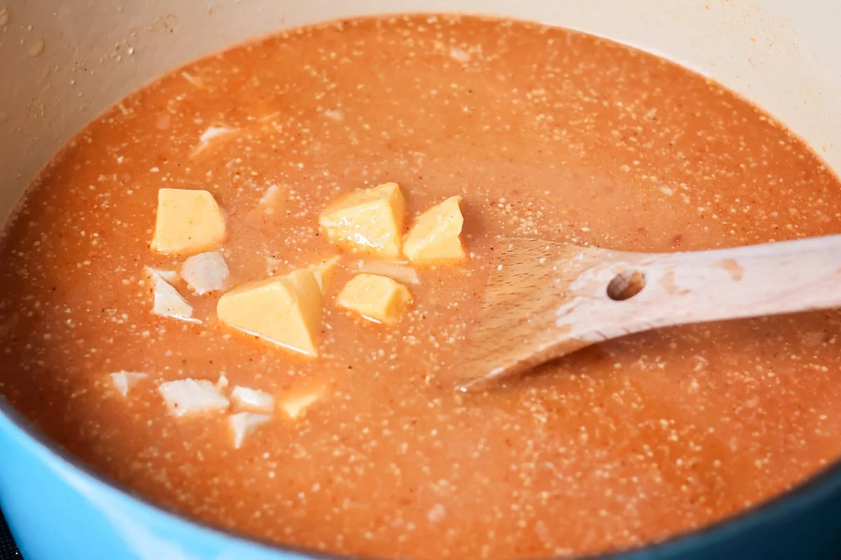 Thick and cheesy Chili's chicken enchilada soup tastes just the original! With mostly shelf-stable ingredients it's our favorite go-to soup. Adding velveeta to the soup in a pot.