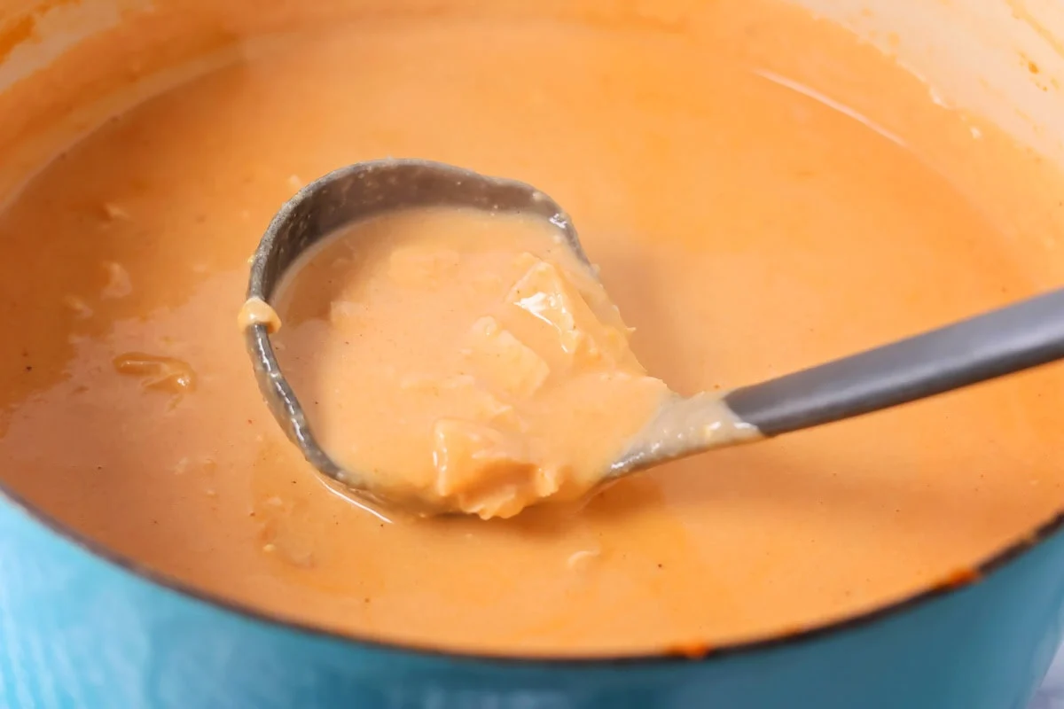 Thick and cheesy Chili's chicken enchilada soup tastes just the original! With mostly shelf-stable ingredients it's our favorite go-to soup. Spooning soup from a dutch oven on the stove.