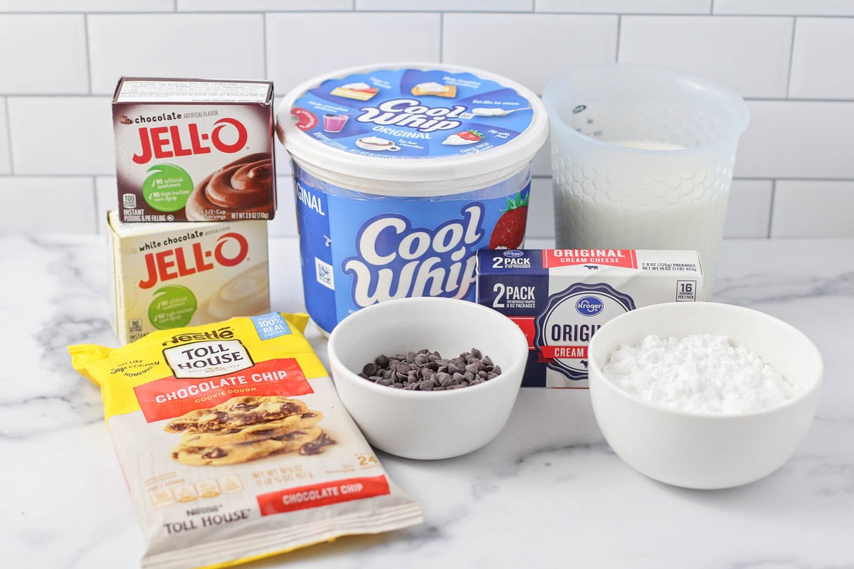 Our chocolate delight recipe features a shortcut cookie crust, creamy pudding, and tangy cream cheese for a delightful layered favorite! Cool whip, pudding, cookie dough, and other ingredients for chocolate delight on a kitchen counter.