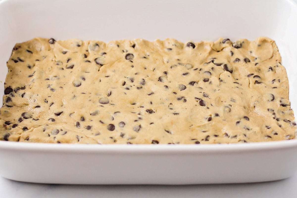 Cookie dough pressed in a white baking dish.