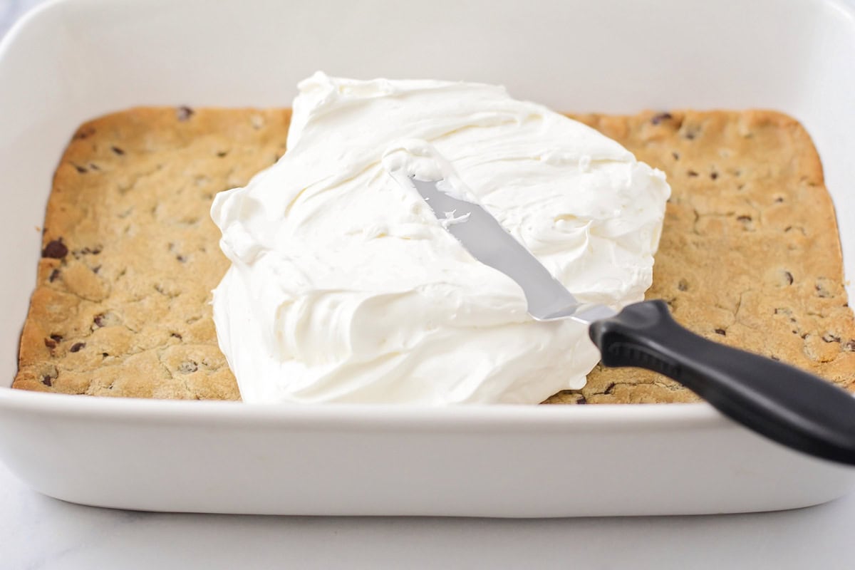 Spreading cream cheese layer of cooled cookie crust.
