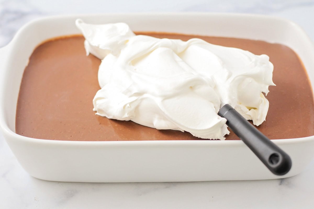 Spreading Cool Whip over the set pudding layer.
