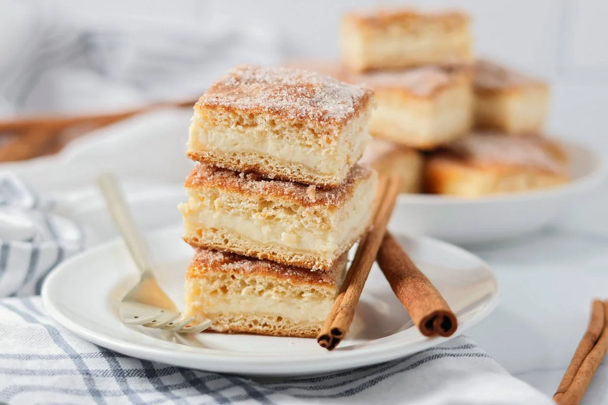 Side view of three squares of churro cheesecake bars stacked on a white plate.