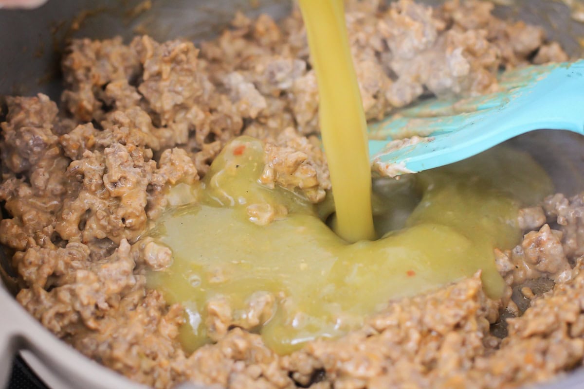 Pouring chili sauce into a pan of browned ground beef.