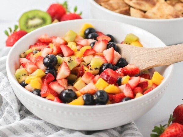A bowl of fresh fruit salsa with a wooden spoon for scooping.