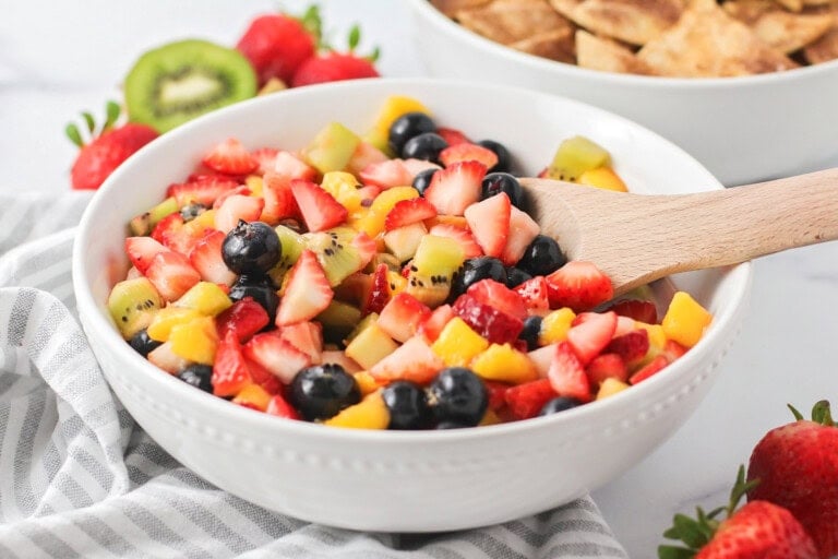 A bowl of fresh fruit salsa with a wooden spoon for scooping.