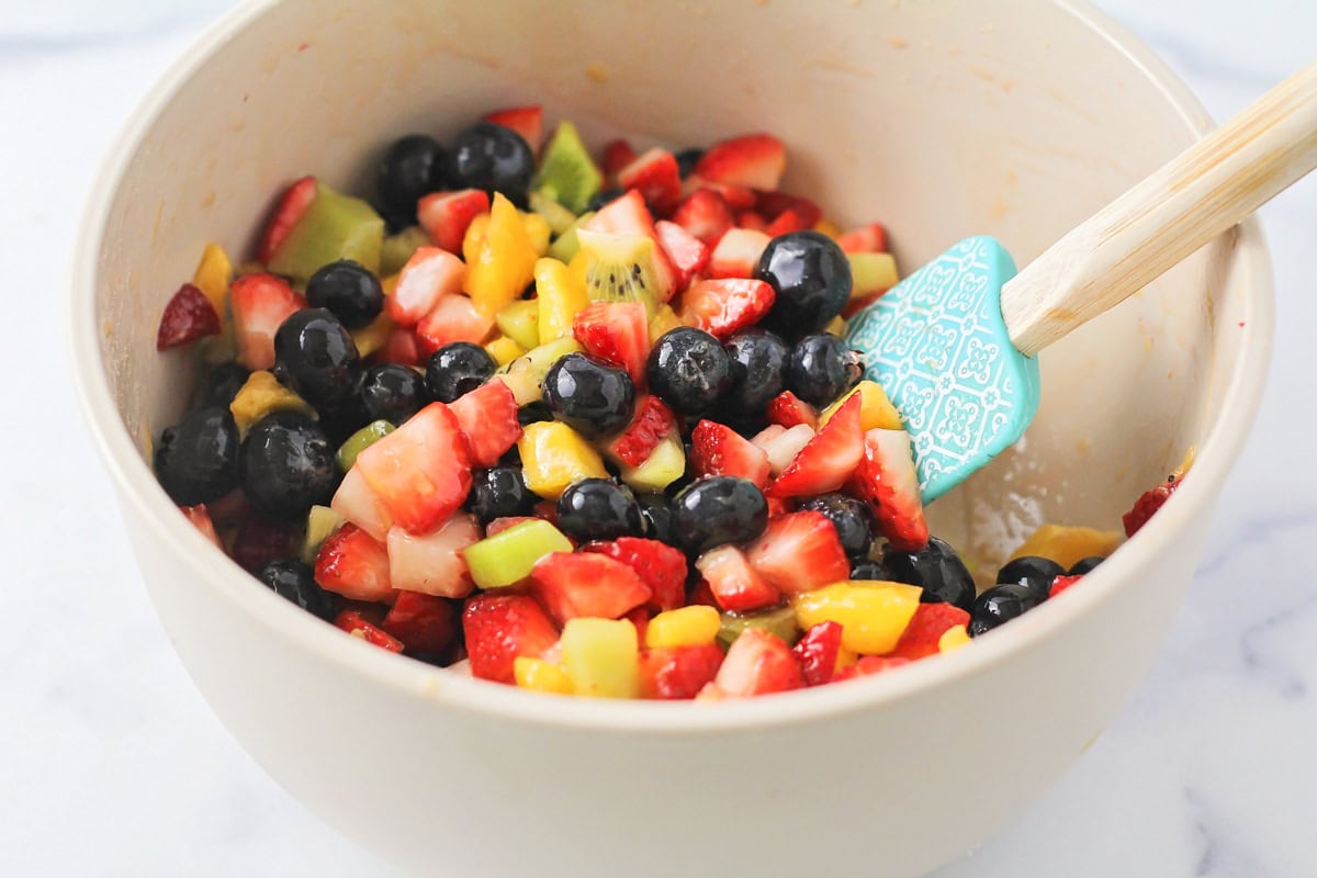 Fresh fruit salsa is a perfect pairing for our sweet homemade cinnamon chips. Ready in under 20 minutes, you can make it for any occasion! Mixing diced fruit in a bowl with a spatula.