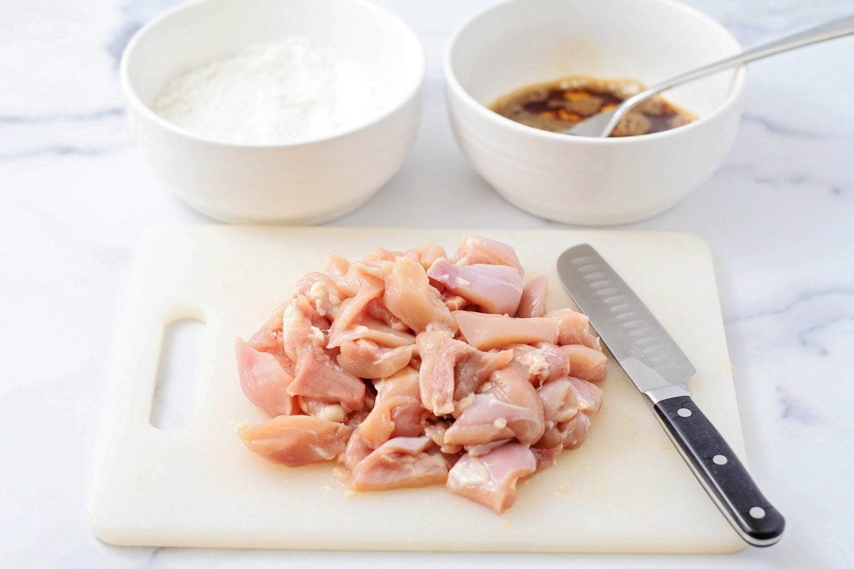 Cut chicken chunks on a cutting board with a knife.