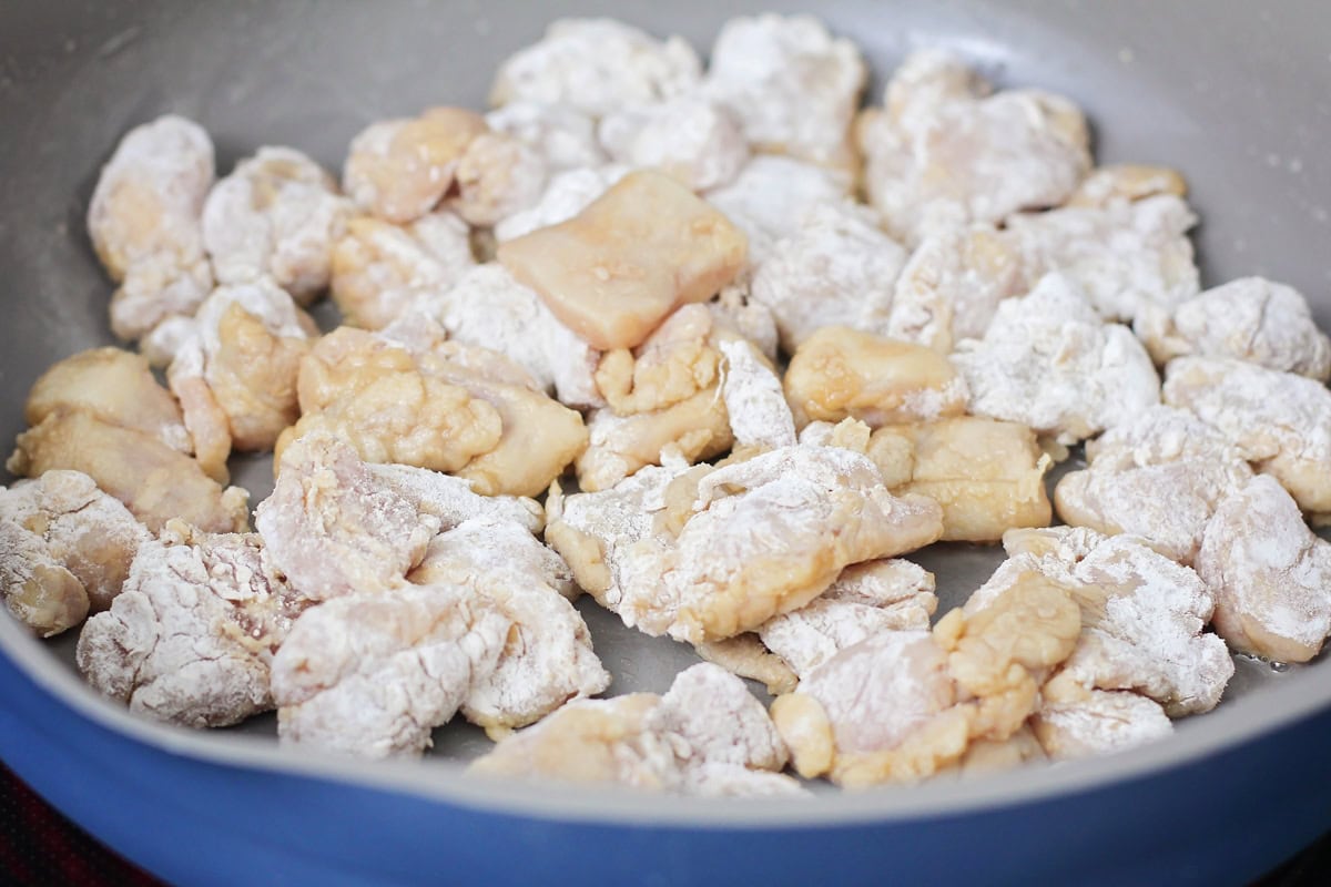 Chicken coated in flour cooking in a skillet of oil.