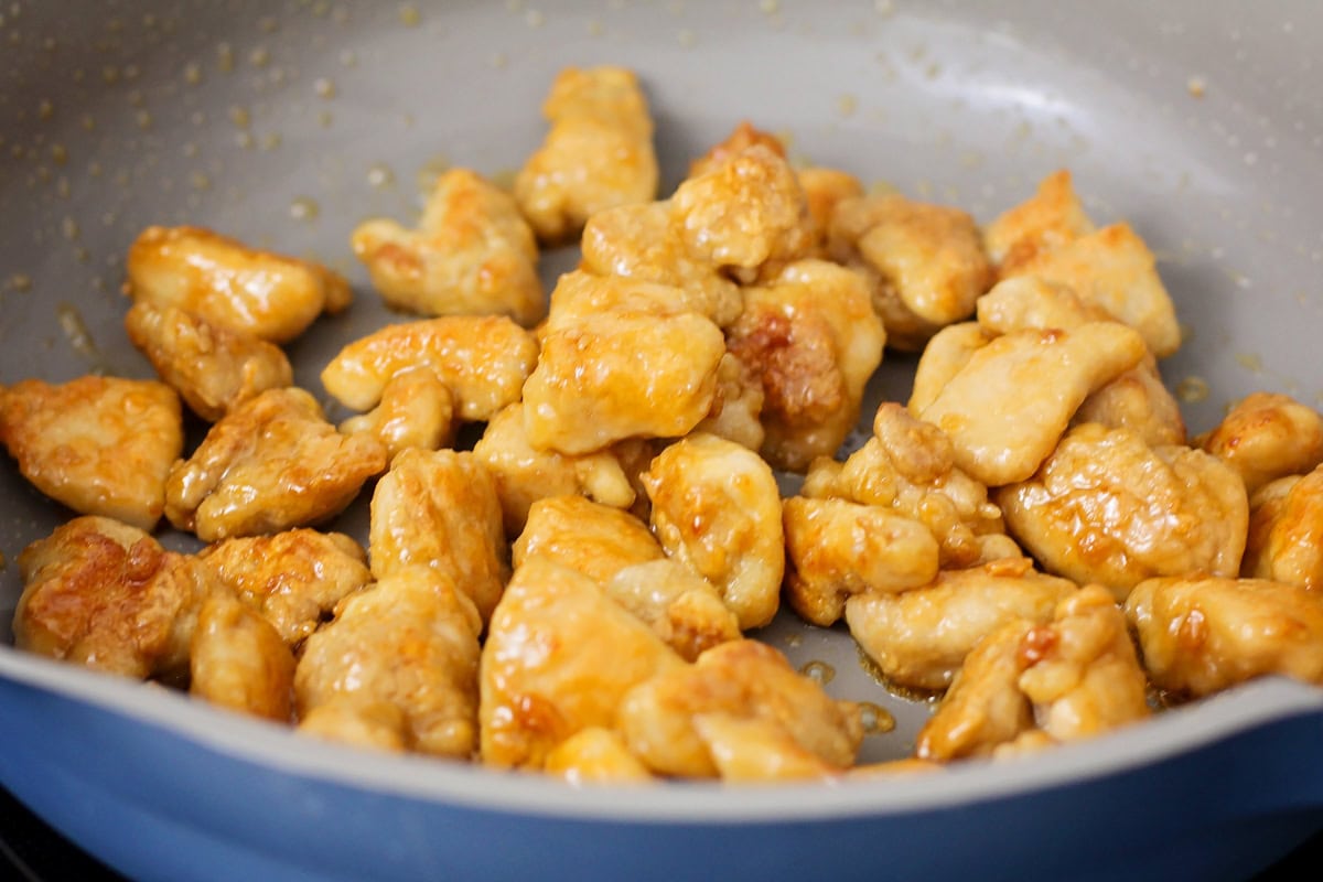 General Tso's chicken coated in a sauce cooking in a skillet.