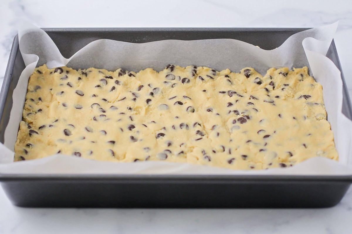 Cookie dough pressed in a lined baking dish.