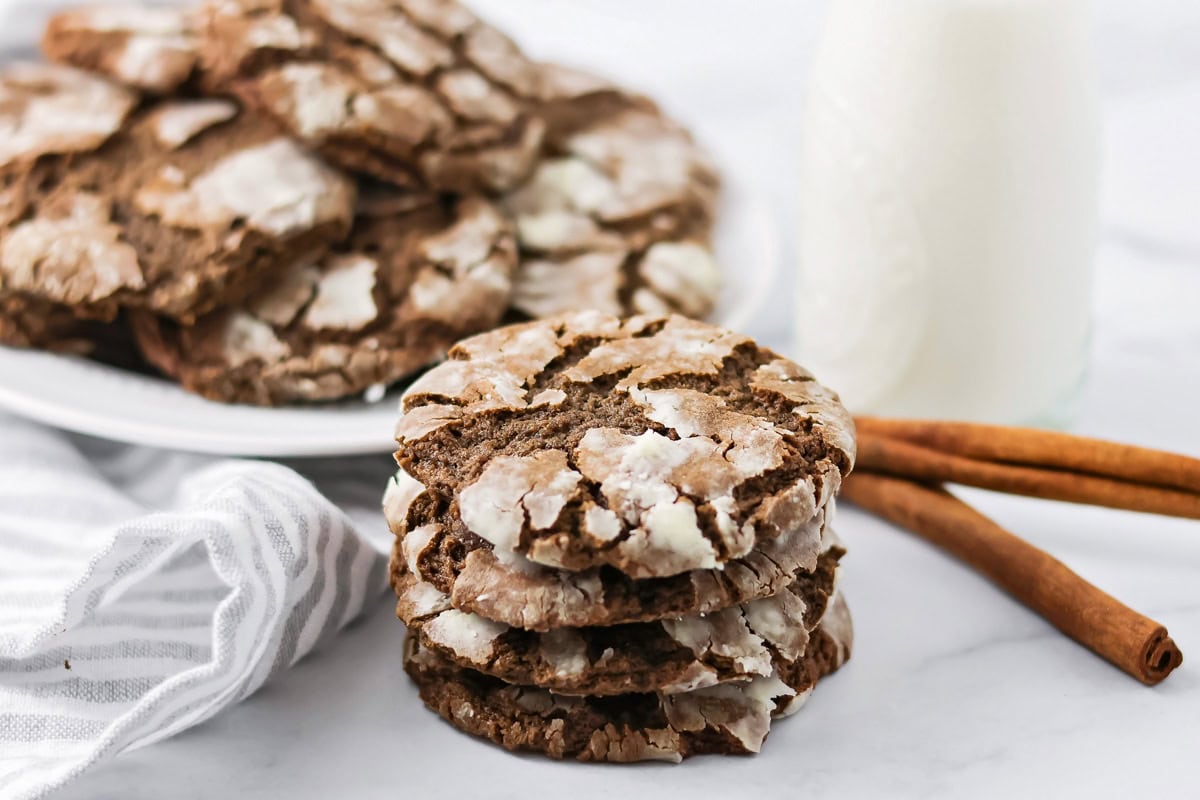 A stack of Mexican crinkle cookies on a kitchen counter with cinnamon sticks.