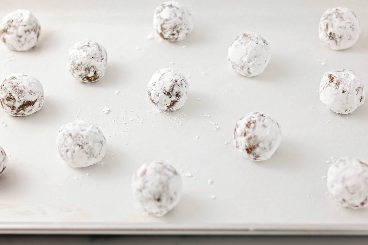 Cookie dough balls dipped in powdered sugar and placed on a lined baking sheet.