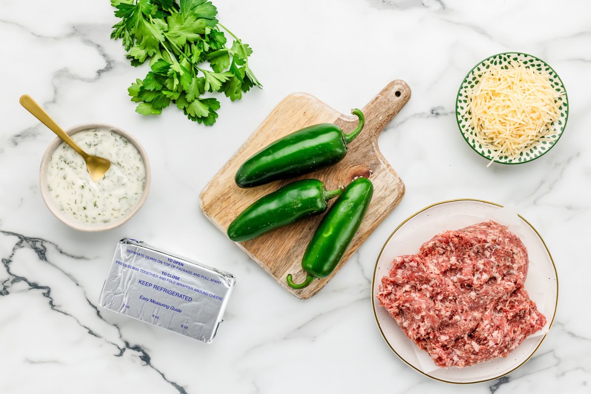 Peppers, sausage, cheese, and herbs on a kitchen counter.