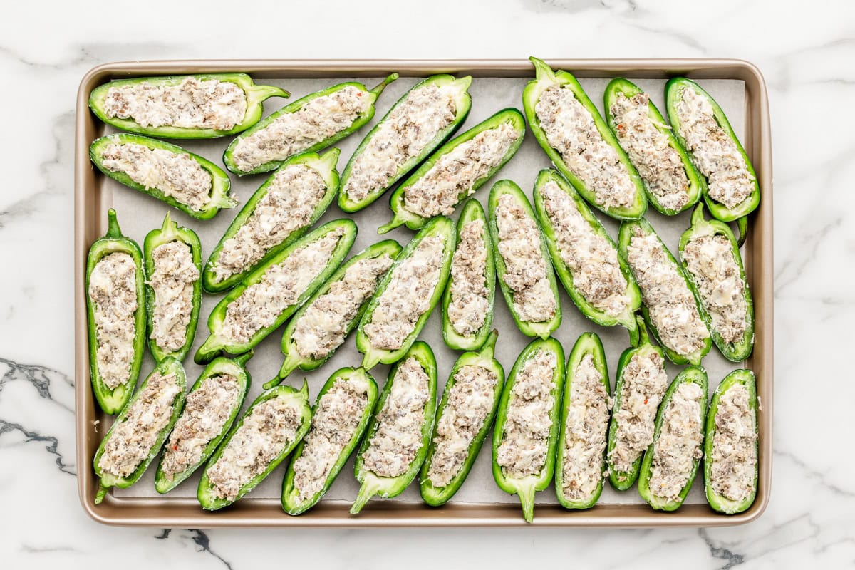 Halved jalapenos filled with the sausage mixture on a baking sheet.