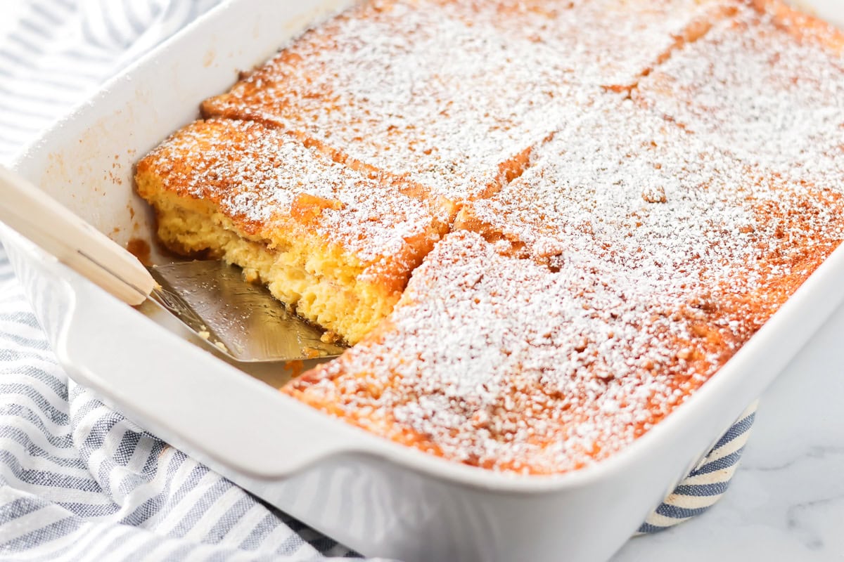 Scooping a serving of Texas toast French toast from a white baking dish.