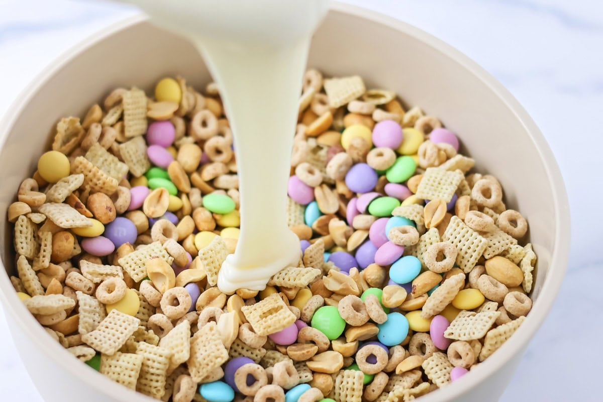 Pouring melted vanilla candy coating over the cereal mixture.