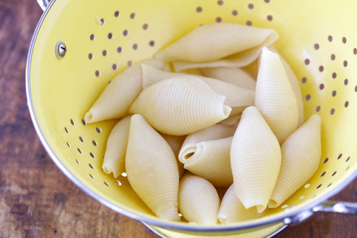 Cooked pasta shells in strainer.