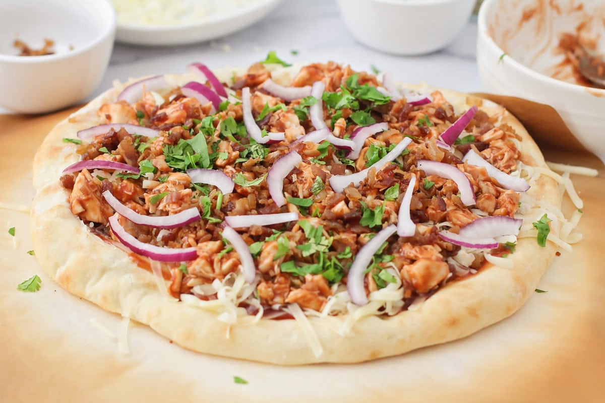 Red onion and herbs on top of the bbq chicken pizza recipe.