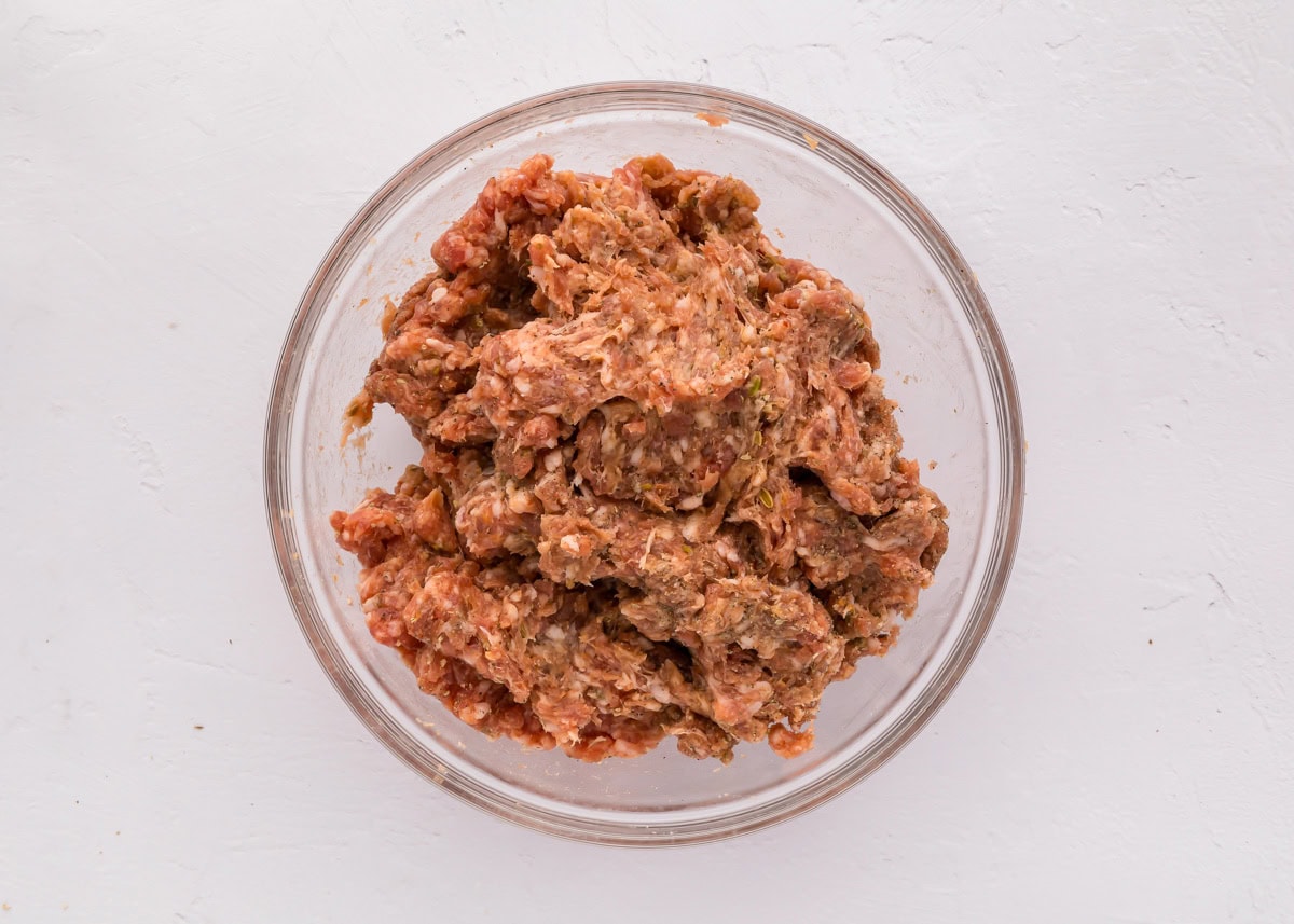 Pork and seasonings mixed in a  glass bowl.
