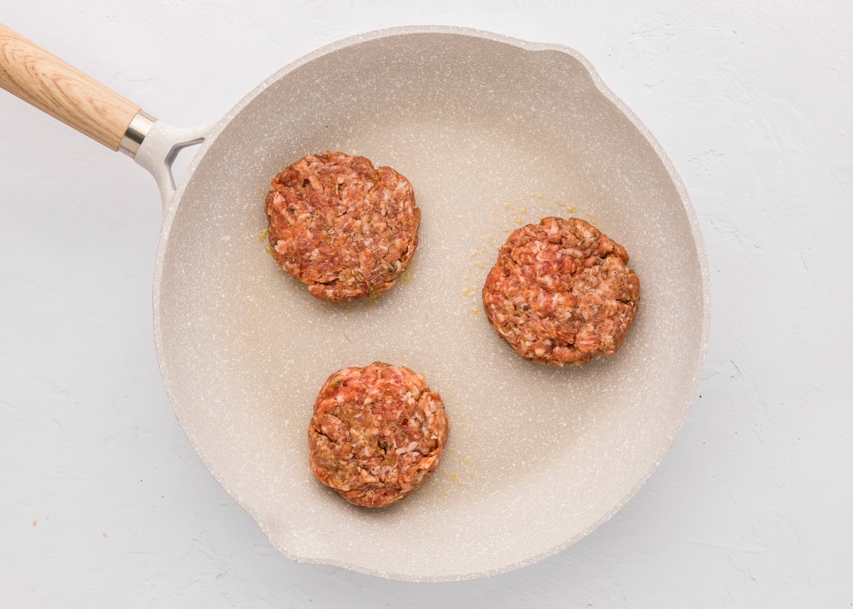 Three sausage patties cooking in a skillet.