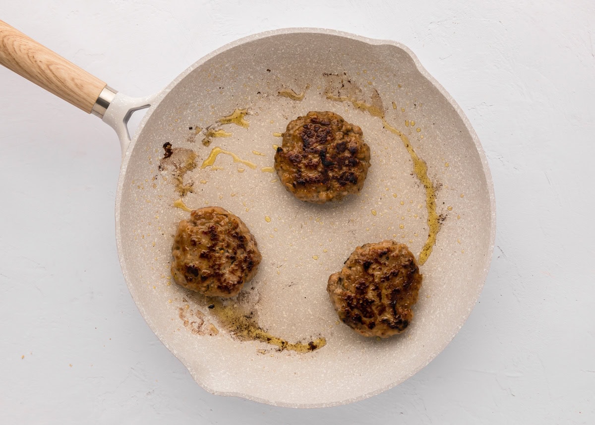 Three sausage patties cooked in a skillet.