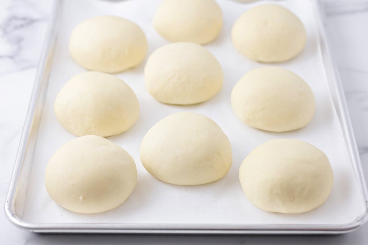 Risen brioche buns on a lined baking sheet.