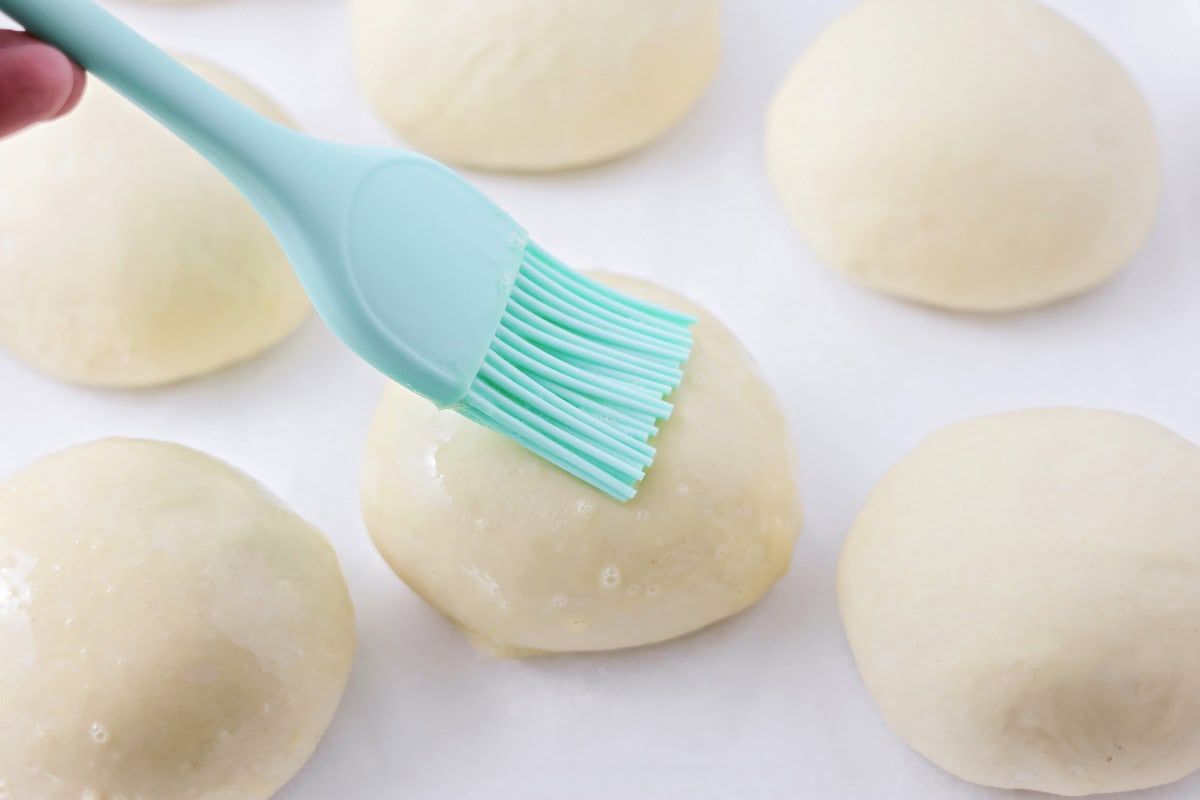 Basting the risen rolls with an egg wash.